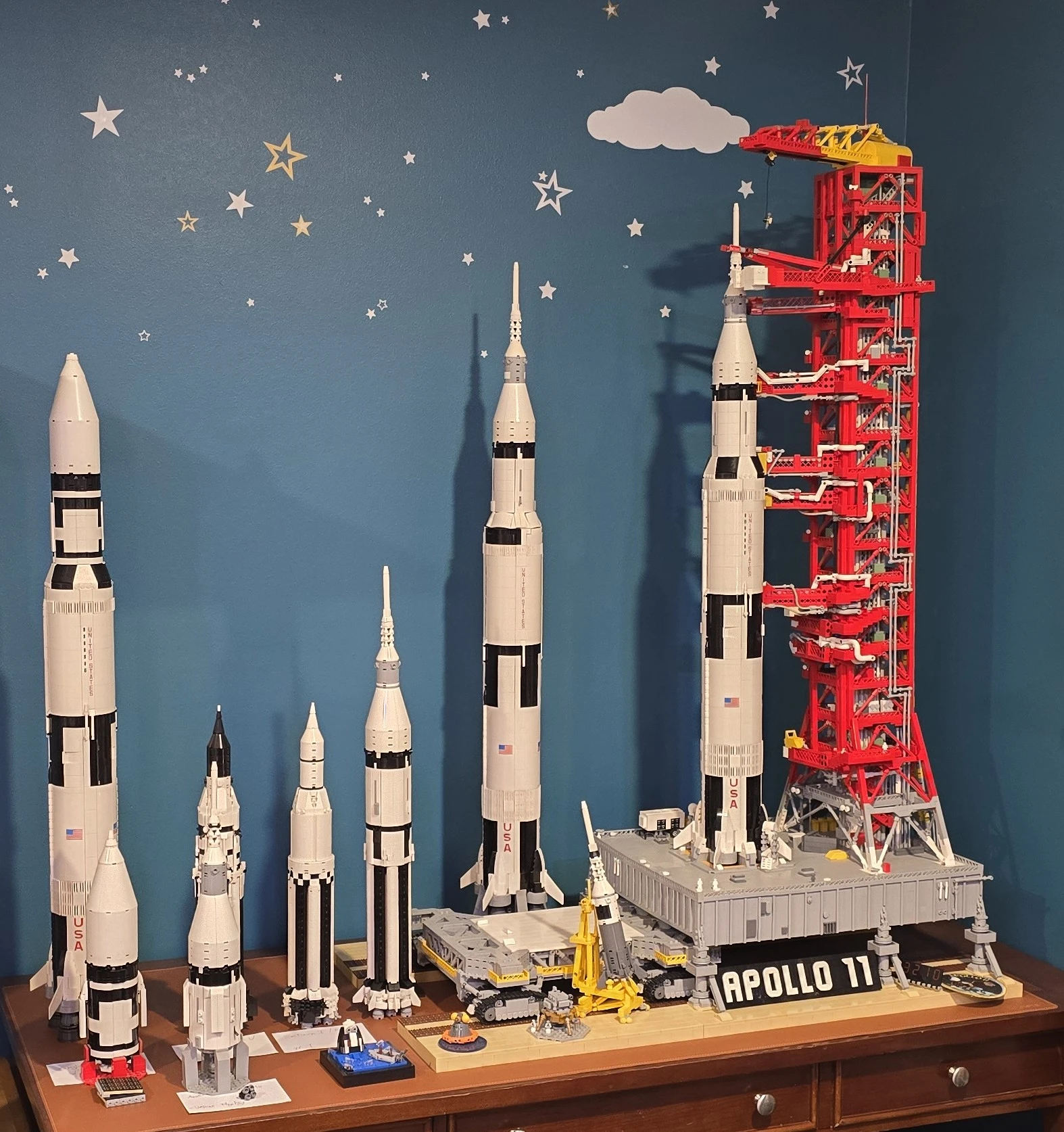 Right to Left: The original Saturn V LEGO set sits atop a custom Launch Tower (LUT) MOC - custom MOCs for the Crawler Transporter, Little Joe II, Saturn V (improved), and several Saturn I launch vehicles.
